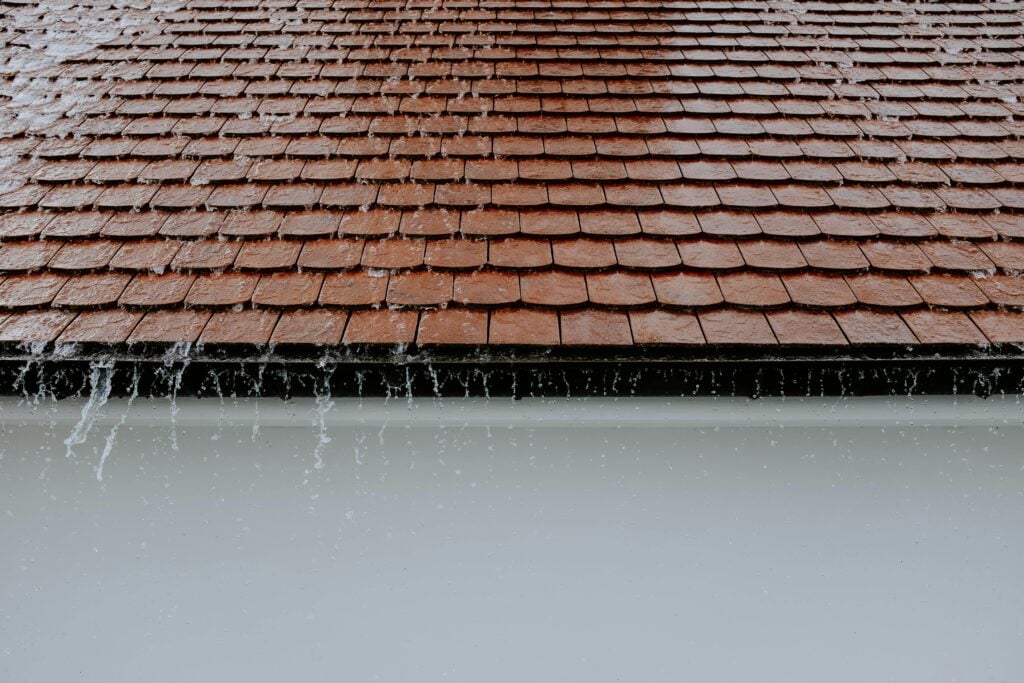 Brown roofing tiles with rainwater cascading down, showcasing architectural texture and detail.